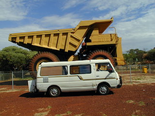 Nissan Camper van parked beside huge mining truck