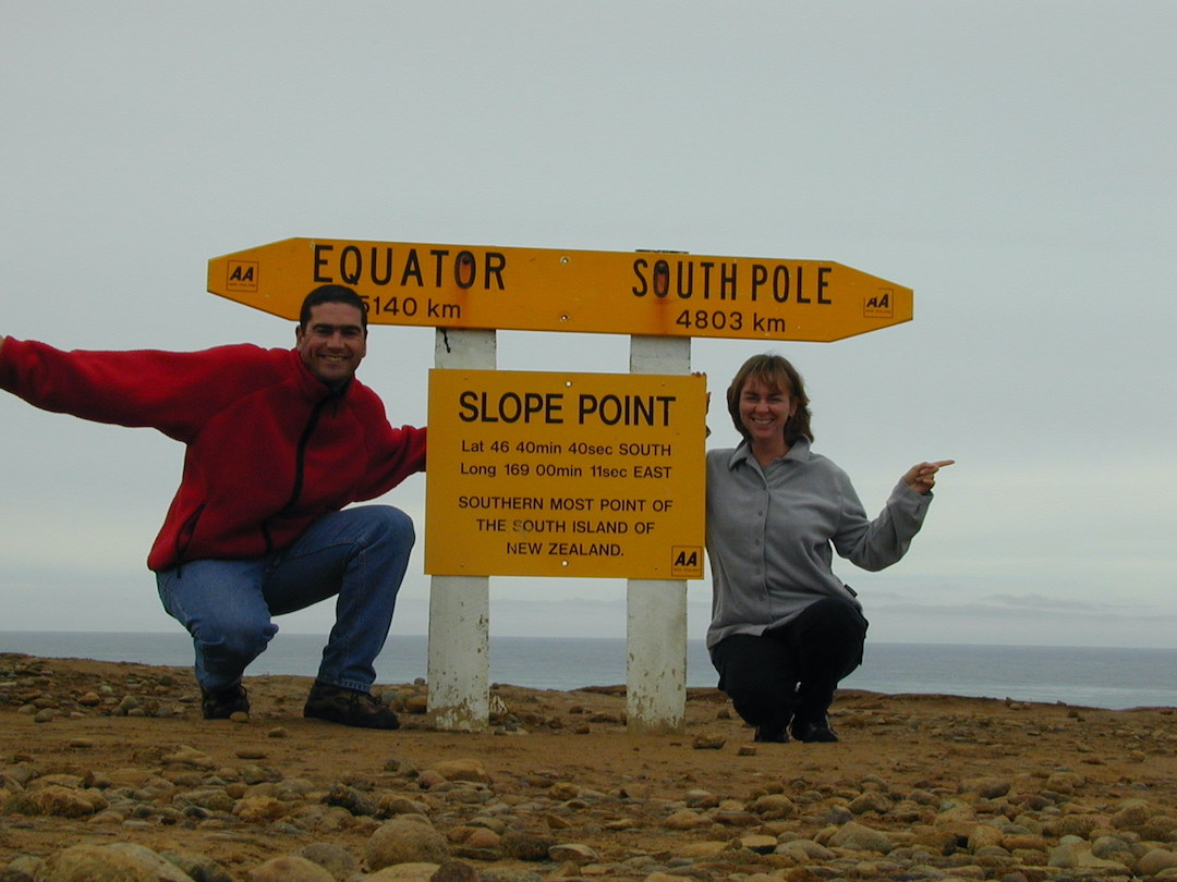 David and Sharon Schindler sitting at Slope Point sign in New Zealand